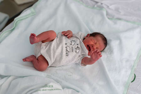 Newborn baby lying on white bed of maternal, infant hospital.