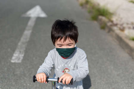 Little boy with medical mask playing with scooter on deserted road with gray vestの写真素材