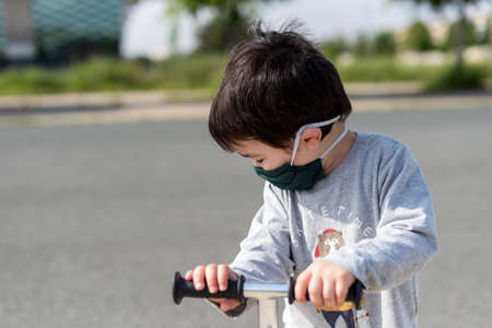 Little boy with medical mask playing with scooter on deserted road with gray vestの写真素材