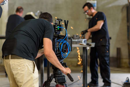 Cameraman with digital film camera filming worker in steel industrial workshop interior