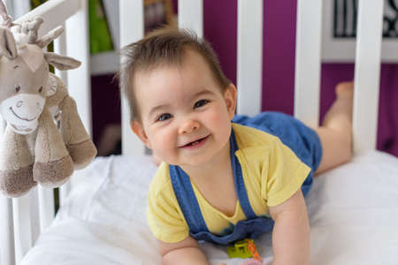 sympathetic baby lying on his stomach in white crib with yellow t-shirt at home