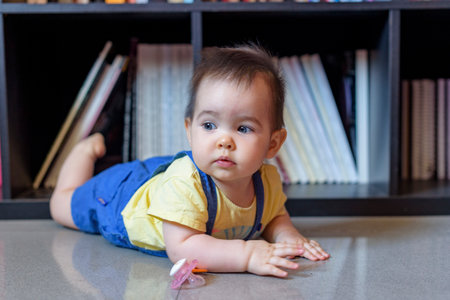 little baby lying on the floor face down with yellow t-shirt in front of booksの写真素材