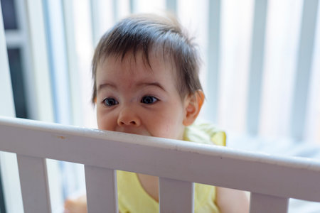 Little baby in white crib with yellow dressの写真素材