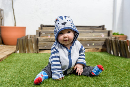 Little baby girl playing sitting on the ground with grass in home garden with hoodieの写真素材