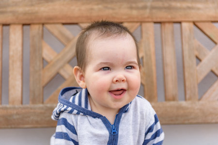Little baby girl playing sitting on wooden bench in home garden with hoodieの写真素材