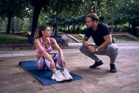 Fitness woman with personal trainer doing exercises on mat outdoors