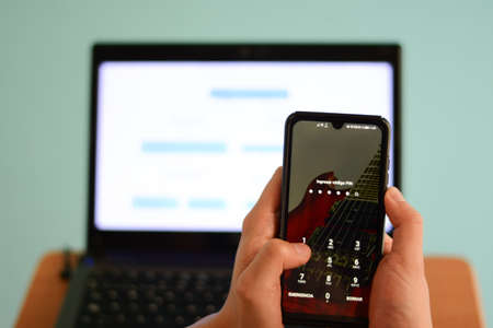 hands holding a phone on background of a laptopの写真素材