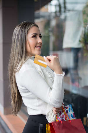 A stylish Hispanic woman with shopping bags and credit card looking at the window of a storeの写真素材