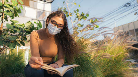Woman with mask reading a book on the streetの写真素材