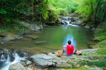 A person rests next to a river and a waterfall with a basket of nuts in the natural park of Gorbeia, Basque Country, Spainの写真素材