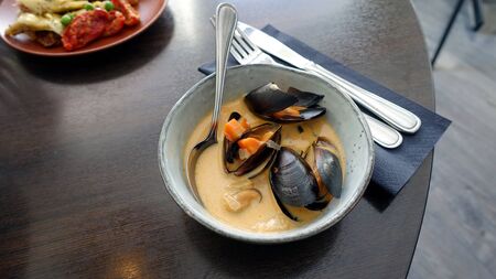 a dish with mussel, shrimp and carrot soup just served at the tableの写真素材
