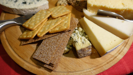 Mixed cow cheeses served on a wooden plate with slices of wholemeal bread
