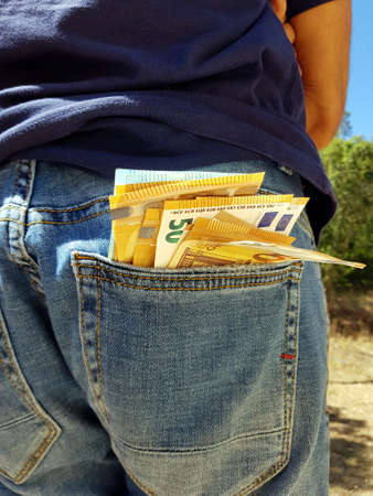 50 and 20 euro banknotes sticking out of the pockets of a person wearing blue jeans