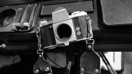 Black and white photo of an antique camera hanging from an old vehicle dashboard.の写真素材