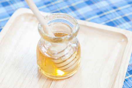 Open glass jar of liquid honey from honey dipper on wood pan and fabric pattern backgroundの写真素材