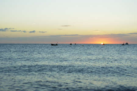 The sun rises in the horizon among the fishing boatsの写真素材