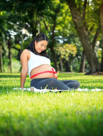 Beautiful pregnant asian woman relaxing in the park with red ribbonの写真素材