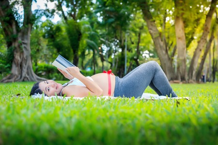 Beautiful pregnant asian woman reading the book in the parkの写真素材