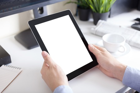 hands of a man holding blank tablet device over a workspace table