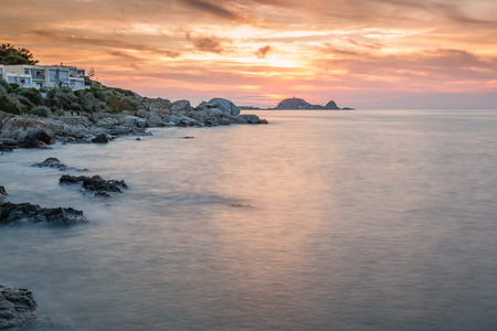 Sunset over Ile Rousse in the Balagne region of Corsica with rocks in foreground