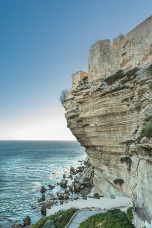 The citadel, wall and houses of Bonifacio in the south of Corsica perched on towering white cliffs and looking down on the evening sun glinting on the Mediterranean seaの写真素材
