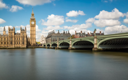 Big Ben and the Houses of Parliament in London with Westminster Bridge and the River Thames in the foreground against a blue sky with fluffy white cloudsのeditorial素材