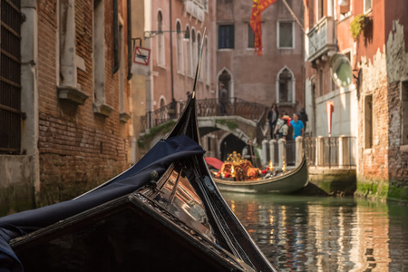 View of a bridge and another gondola shot from within a gondola on a canal in Venice on a bright sunny day showing front of the gondola in the foregroundの写真素材