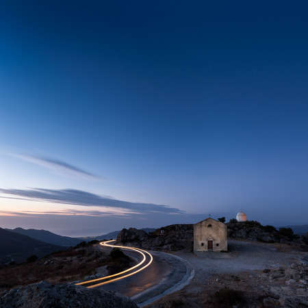 Car light trails curve around the mountain road past the San Sebastiano chapel and mausoleum near Palasca in the Balagne region of Corsica as dusk fallsの写真素材
