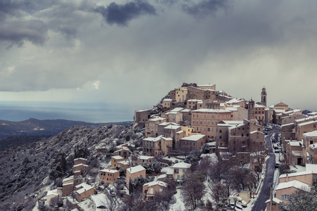 Snow and dark clouds cover the ancient mountain village of Speloncato in the Balagne region of Corsicaの写真素材