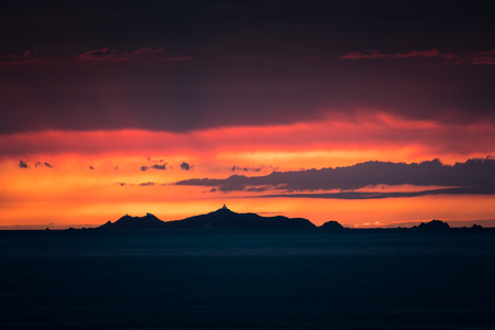 Lighthouse and rocks of Les Iles Sanguinaires near Ajaccio in Corsica silhouetted against a bright orange sunsetの写真素材