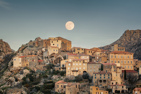 Full moon rising over the houses of the mountain village of Speloncato in the Balagne region of Corsica as the last of the sun goes downの写真素材