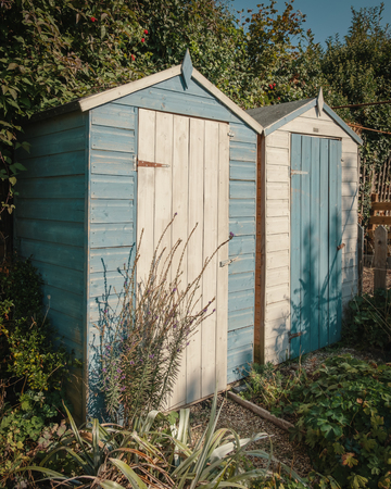 Two small wooden garden sheds standing next to each other painted in white and pale blueの写真素材