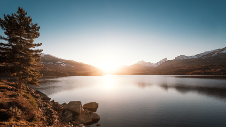 Sun setting behind snow capped mountains at Lake Calacuccia in central Corsicaの写真素材