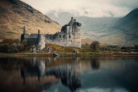 Kilchurn Castle reflected in a still Loch Awe in the Highlands of Scotland with early morning clouds sitting on the distant hillsの写真素材