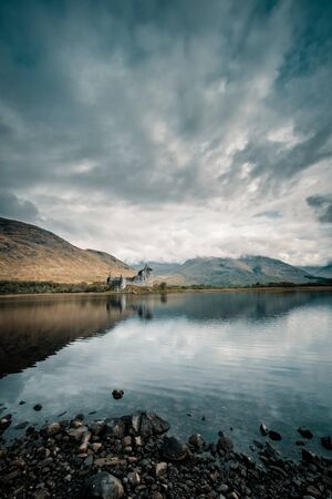 Kilchurn Castle reflected in a still Loch Awe in the Highlands of Scotland with early morning clouds sitting on the distant hillsの写真素材