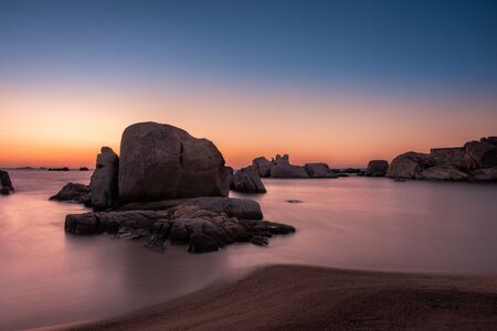Long exposure image of dramatic orange & purple sunrise over the Mediterranean sea and large granite boulders on the coast of Cavallo Island n the Lavezzi archipelago of Corsicaの写真素材