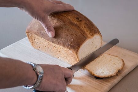 Woman cutting into a freshly baked loaf of crusty white bread sitting on a wooden bread board