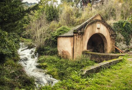 Ancient stone wash house standing by a fast flowing stream in the ancient mountain village of Ville di Paraso in the Balagne region of Corsicaの写真素材