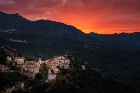 Dramatic orange sunset over the mountain village of Belgodere in the Balagne region of Corsicaの写真素材