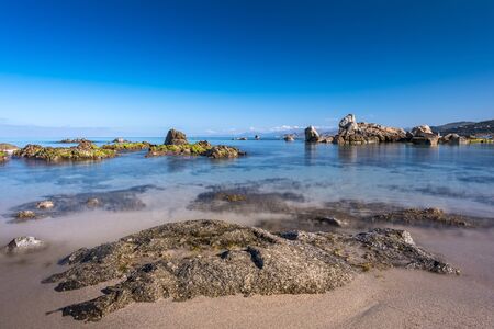 Rocks along the beach and a calm Mediterranean sea near L'Ile Rousse in the Balagne region of...