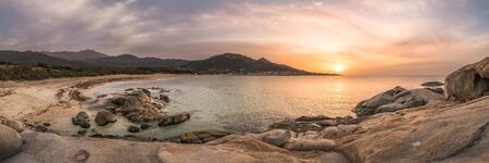 Panoramic view of sun setting over rocky coastline and sandy beach of the village of Algajola in the...