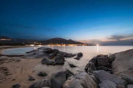 Night falling over rocky coastline and sandy beach with the village of Algajola in the Balagne region of Corsica in the distanceの写真素材