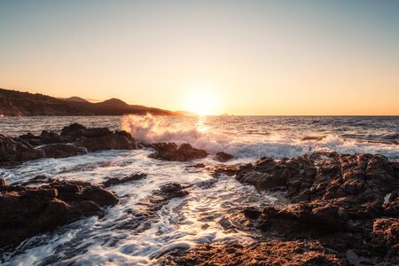 Waves crashing onto the rocky coastline of Corsica as the sun sets over the Balagne town of Ile Rousseの写真素材
