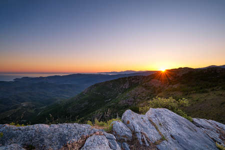 Sun rising over Cap Corse and the coastline of Corsica with a rocky outcrop in the foregroundの写真素材