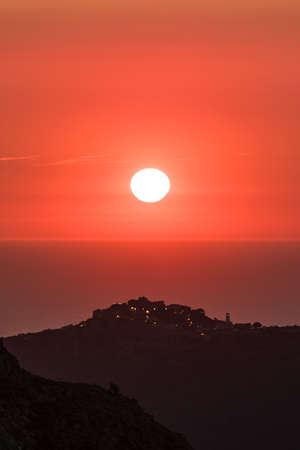 Orange afterglow after the sun has set over the Mediterrnean sea with the silhouetted hilltop village of Sant'Antonino in Corsica in the foregroundの写真素材