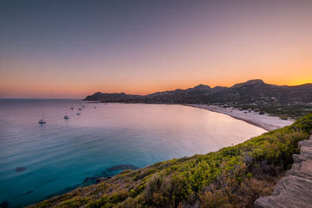 Boats moored in the bay as dawn is breaking over the beach at Ostriconi in the Balagne region of Corsica with the Desert Des Agriates in the distanceの写真素材