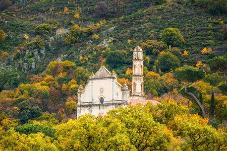 The facade and bell tower of the church at Ville Di Paraso in the Balagne region of Corsica surrounded by autumnal treesの写真素材