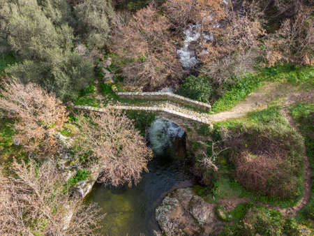 Aerial view of a mountain stream rushing through a woodland and cascading beneath an ancient Genoese bridge near Feliceto in the Balagne region of Corsicaの写真素材