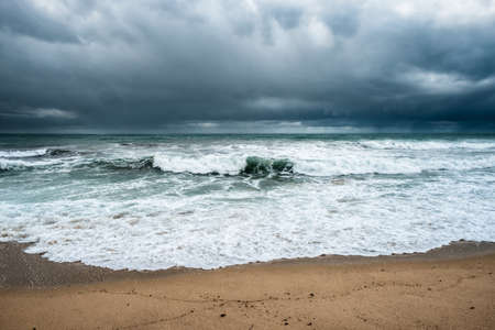 Rough seas crash onto the beach at Algajola in the Balagne region of Corsica with dark clouds and rain over the horizonの写真素材