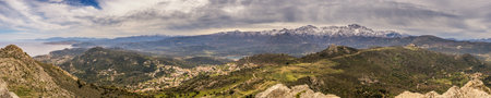 Panoramic view over the villages of the Balagne region of Corsica, the Mediterranean coastline with snow capped mountains in the distanceの写真素材